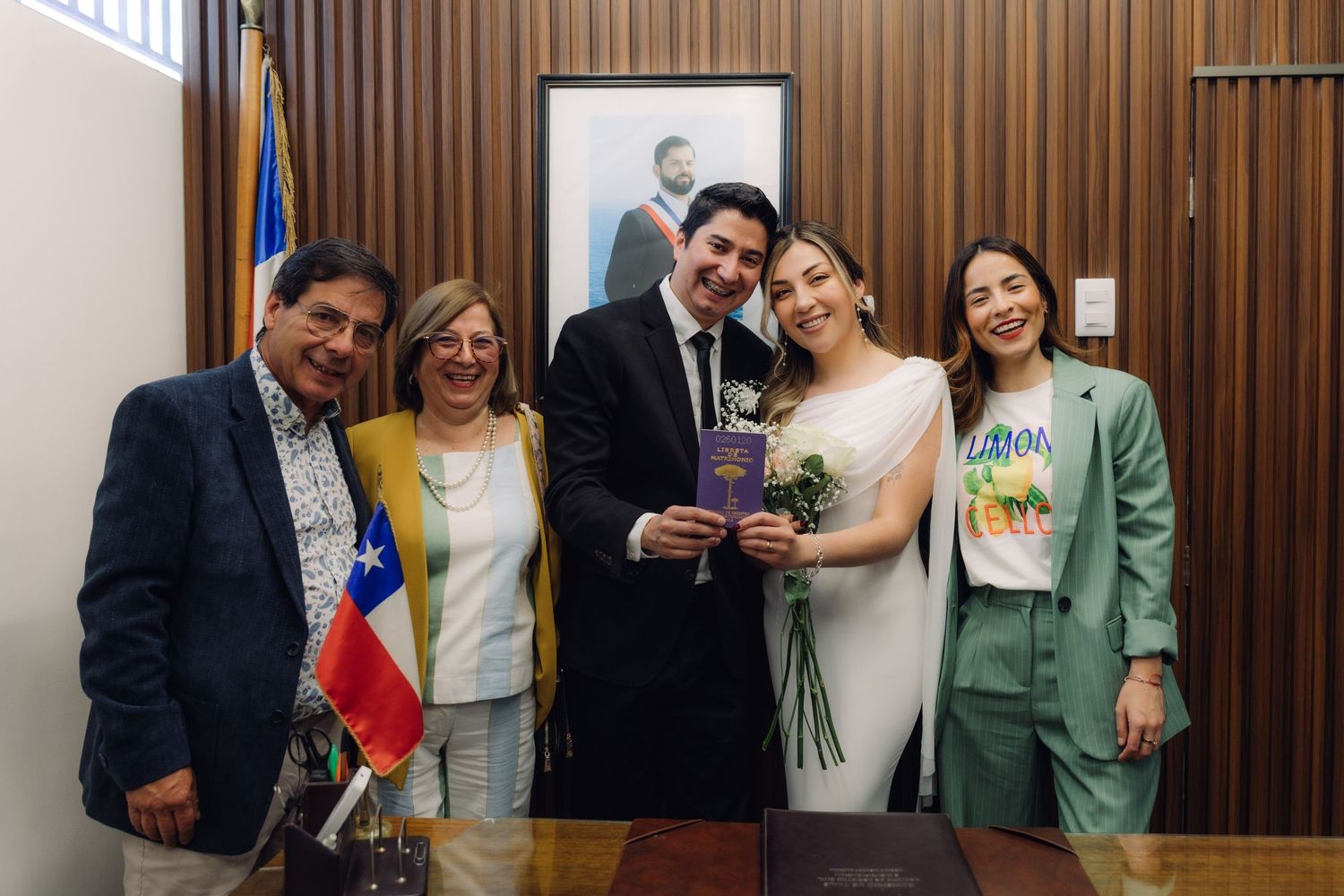 Smiling newlyweds posing with three guests holding marriage certificate at Chilean civil ceremony.