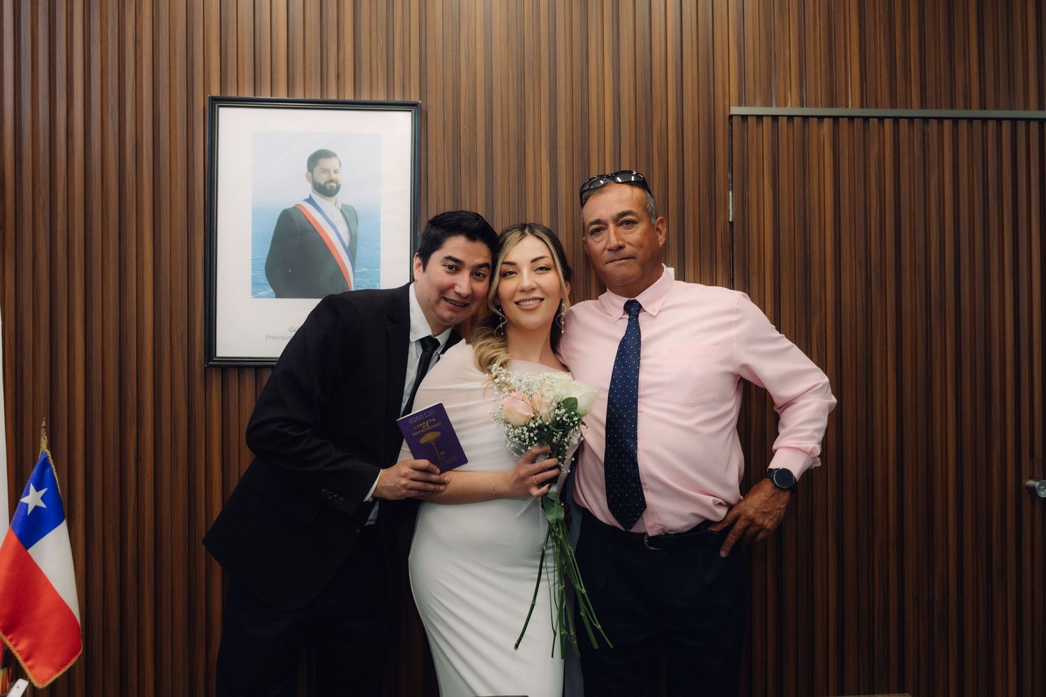 Laughing newlyweds making peace signs in front of presidential portrait at Chilean civil wedding.