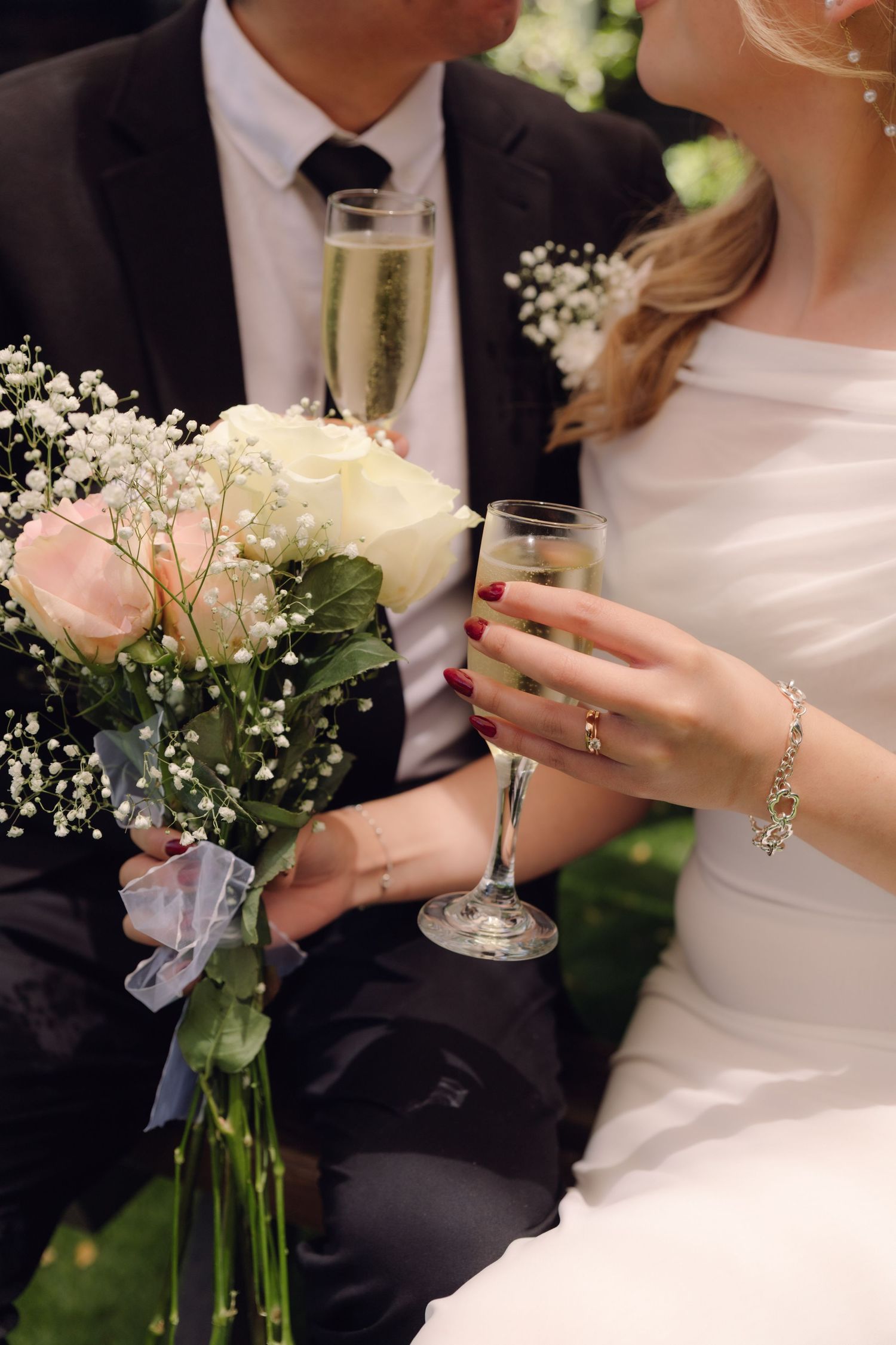Close-up of bride and groom holding champagne glasses with a wedding bouquet of roses and baby's breath.