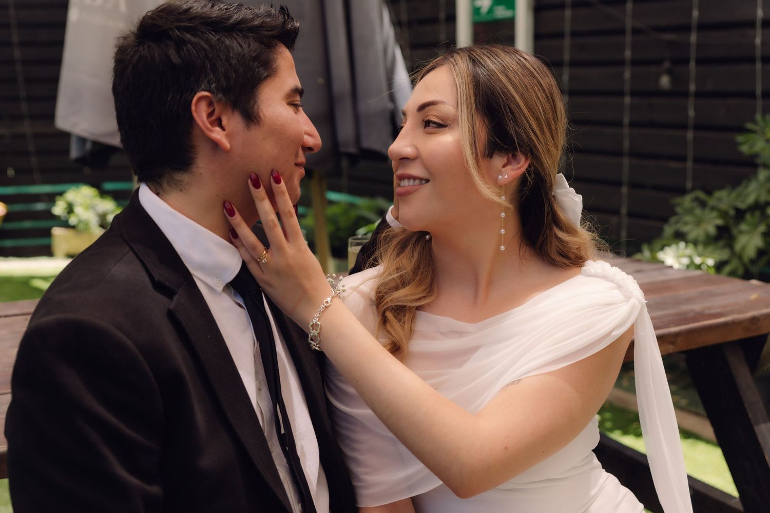 Smiling bride touching groom's face tenderly while sitting together at their wedding celebration.