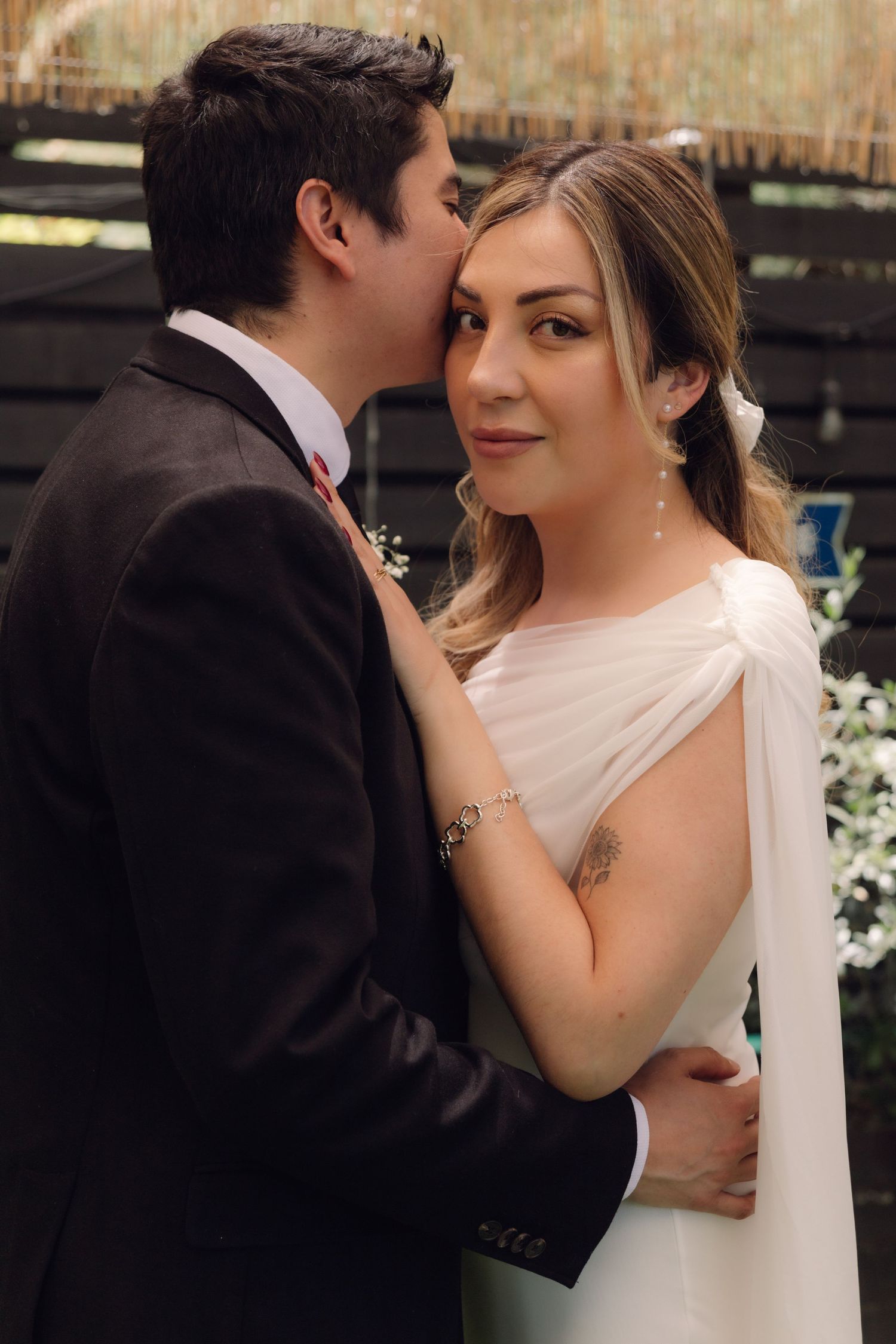 Groom kissing bride's cheek while she gazes softly forward, wearing elegant drop earrings and white gown.