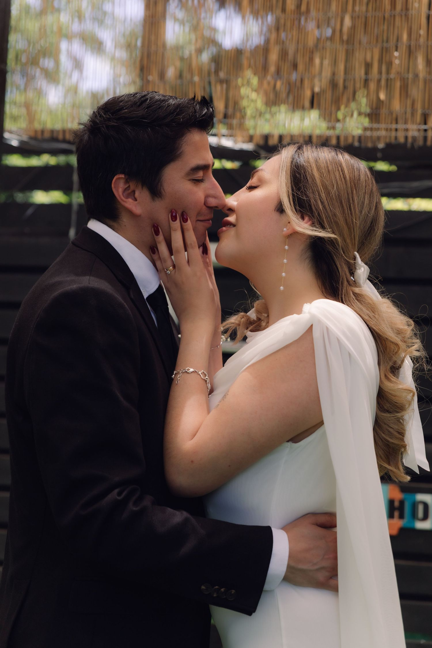 Bride and groom sharing romantic kiss at outdoor wedding, bride in elegant white cape dress, groom in black suit.