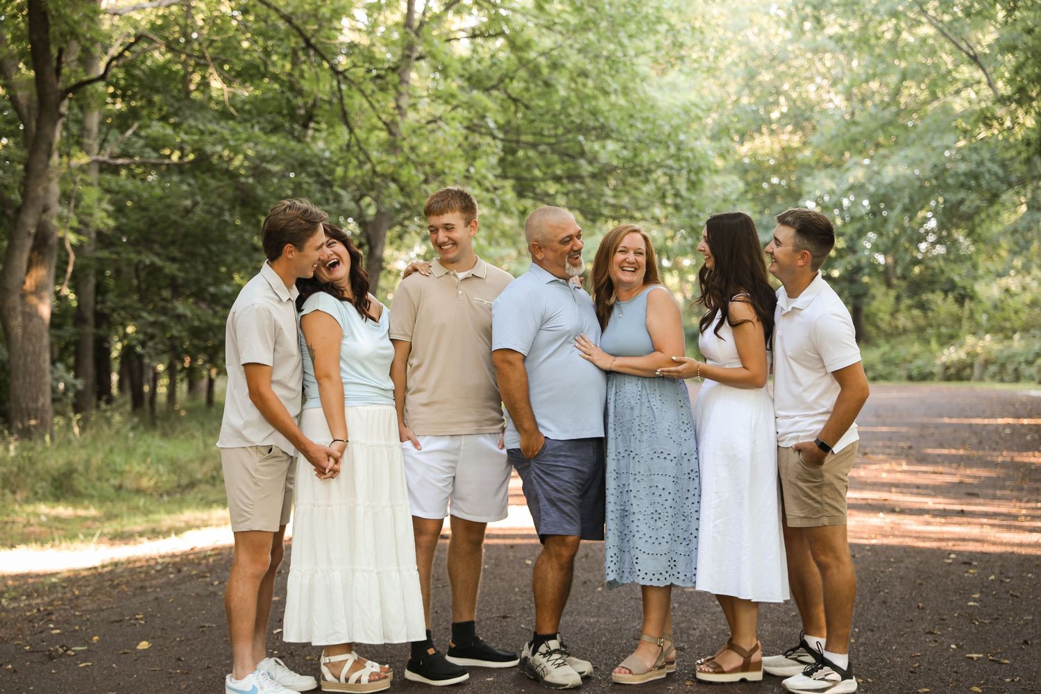 Family of six smiling and laughing together on a tree-lined path during an outdoor portrait session.