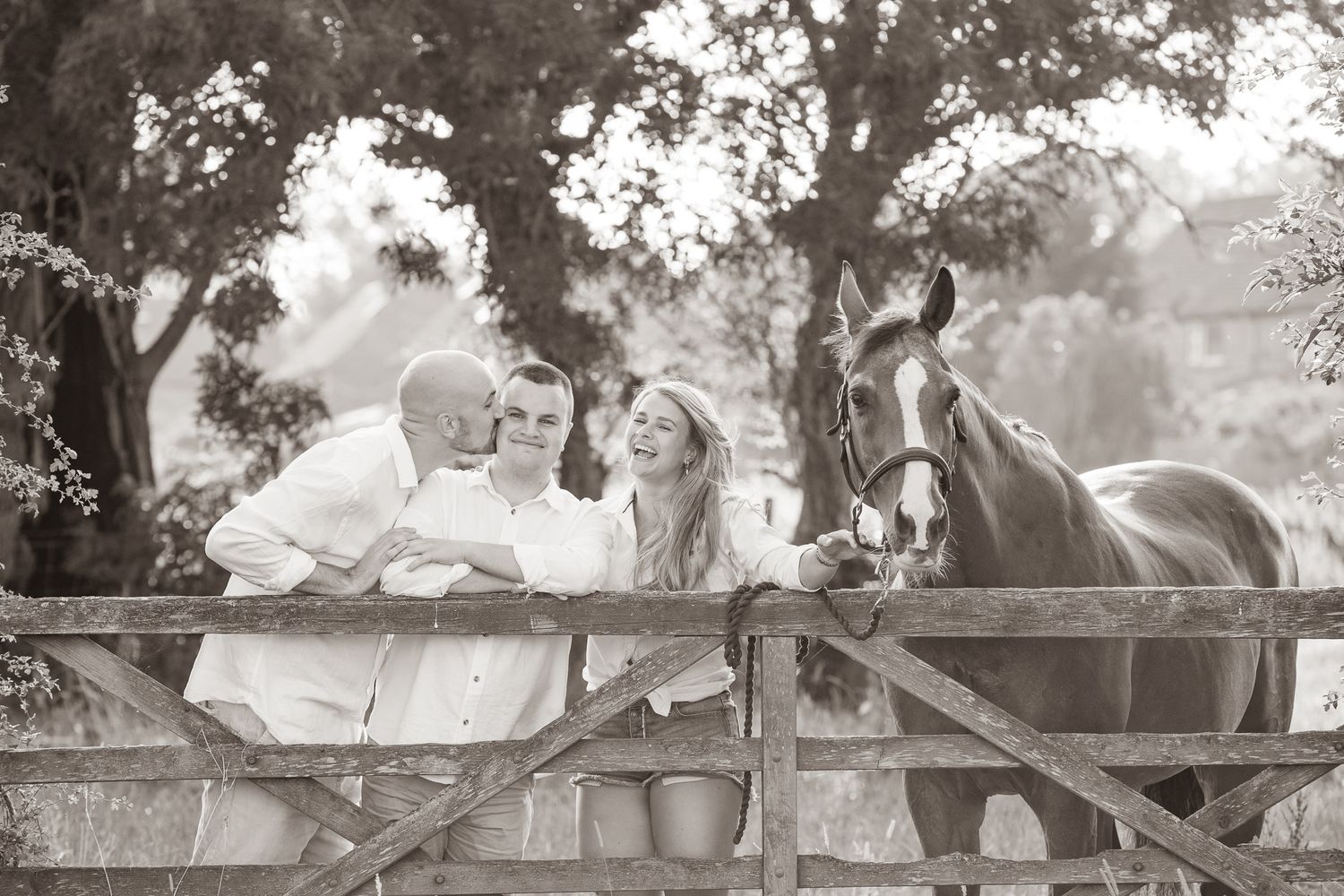 Two riders stand with their animals - a dog and a dark horse relaxing outdoors in a black and white photo.