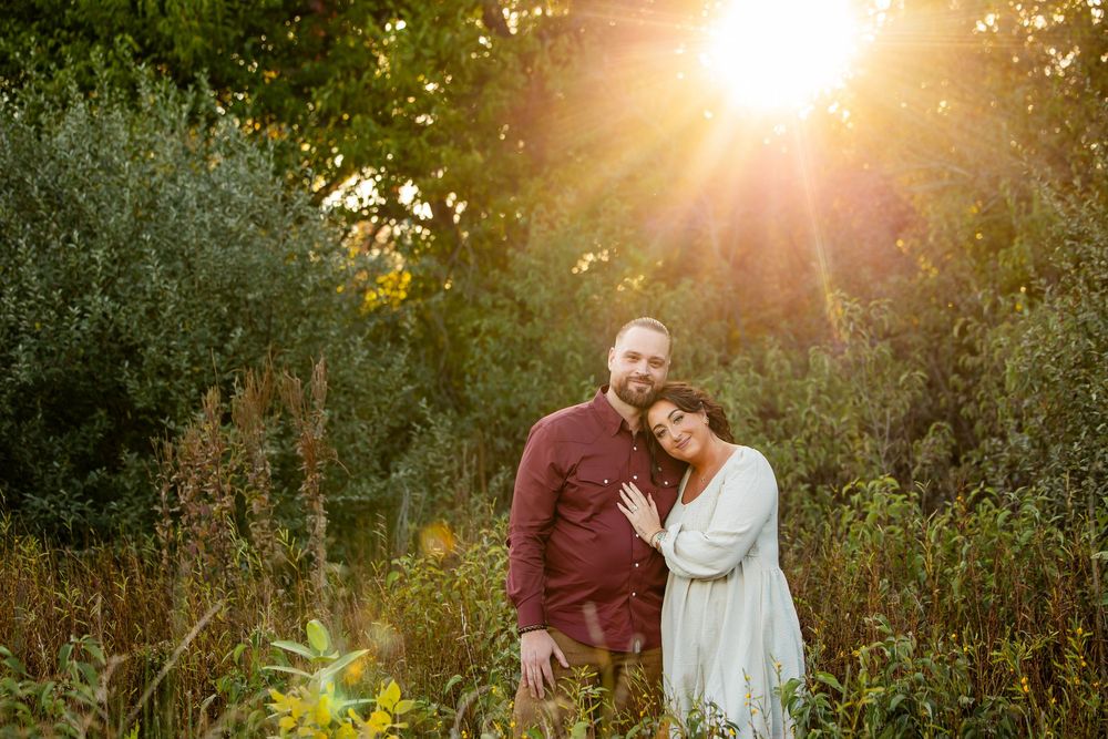 Couple embracing in lush green field during golden sunset, man in red shirt, woman in mint dress, romantic outdoor portrait.