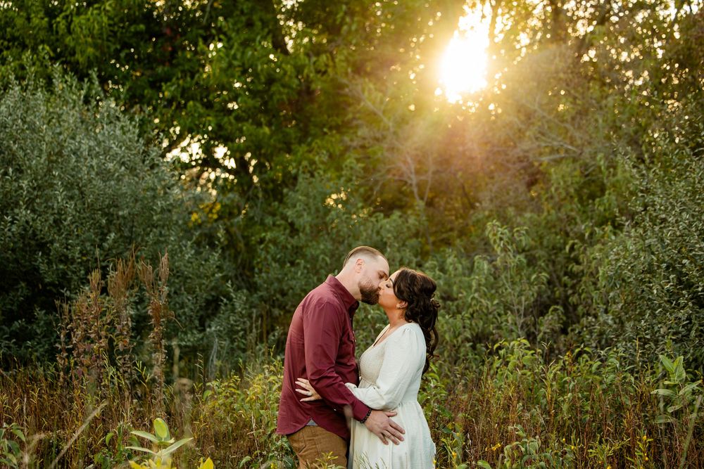 Couple sharing a romantic moment at golden hour surrounded by lush green foliage in an outdoor setting.