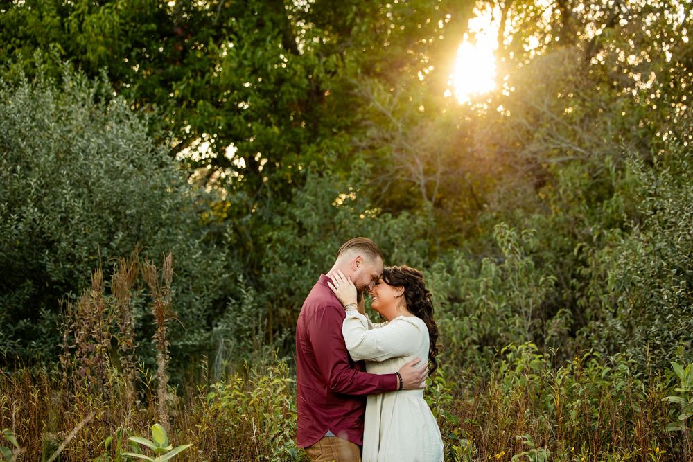 Couple embracing at golden hour sunset in lush green forest meadow, romantic engagement photo.