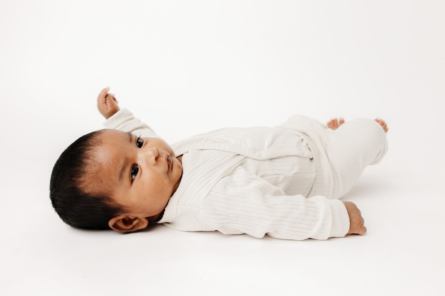 Peaceful newborn baby sleeping on white blanket, dark hair, soft skin, serene expression, professional newborn photography.