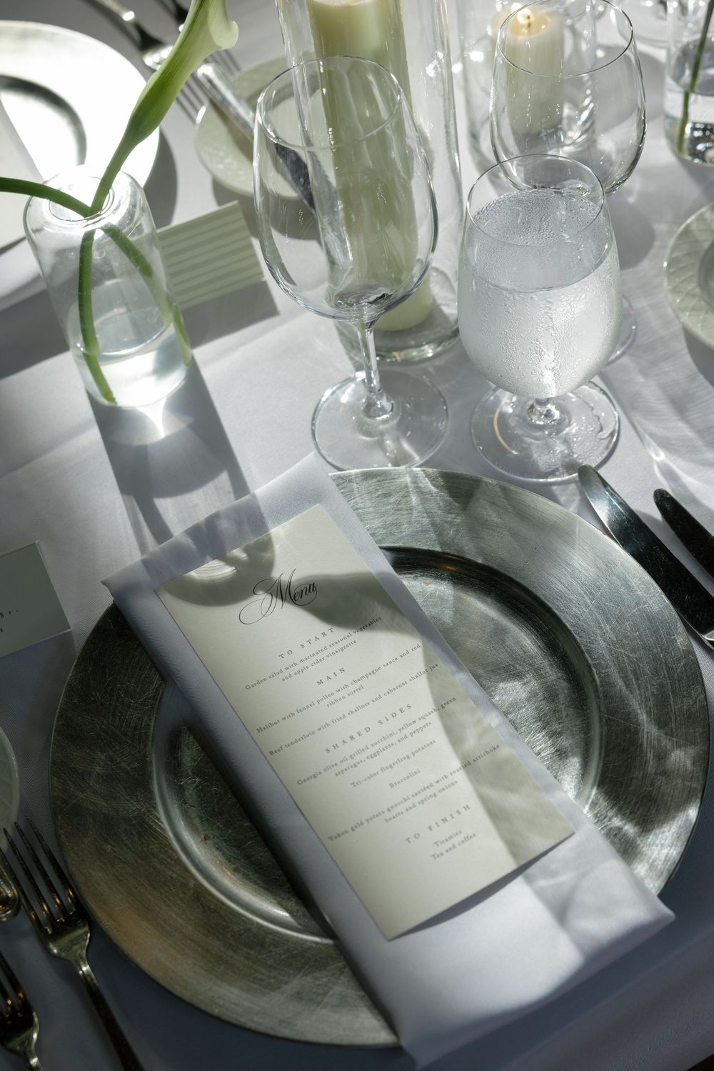 Elegant wedding table setting with a silver charger plate, printed menu card, folded napkin, and crystal glassware.