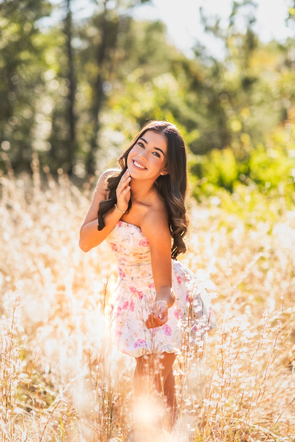 Young woman in floral dress standing in golden field with sunlight, smiling outdoors.