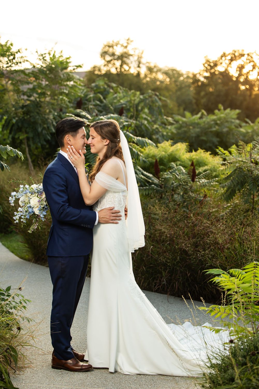 Bride and groom share a romantic moment in a lush garden at golden hour, bride in white gown with veil.