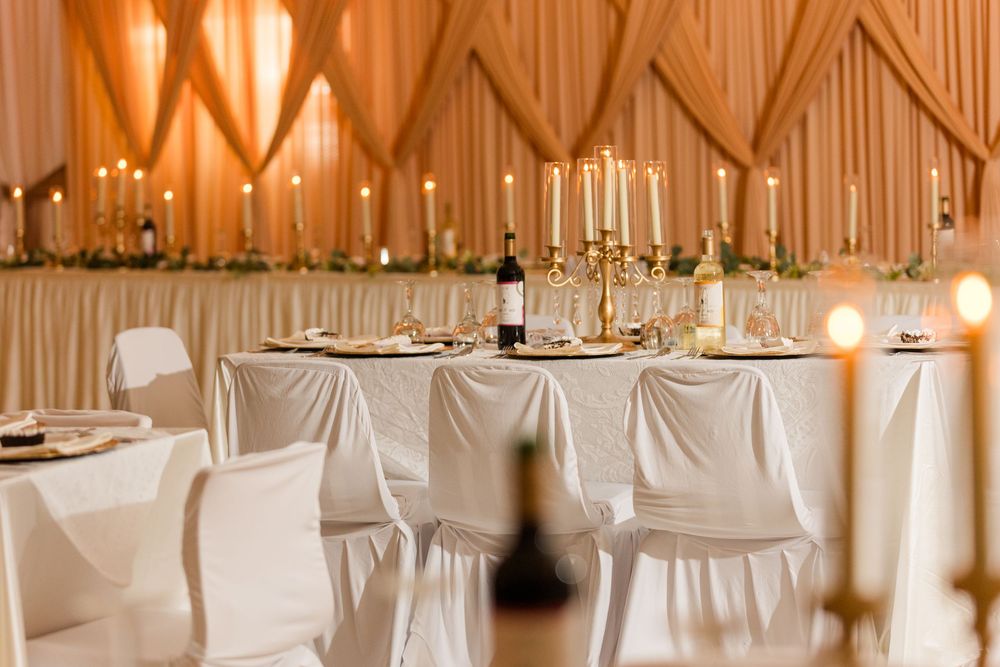 Elegant wedding reception venue with white chair covers, gold candelabras, and draped peach fabric ceiling decor.