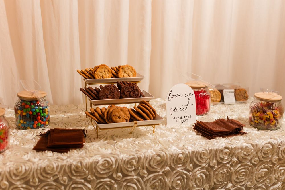 Elegant wedding dessert table with cookies, brownies, and candy jars on a white rosette tablecloth.