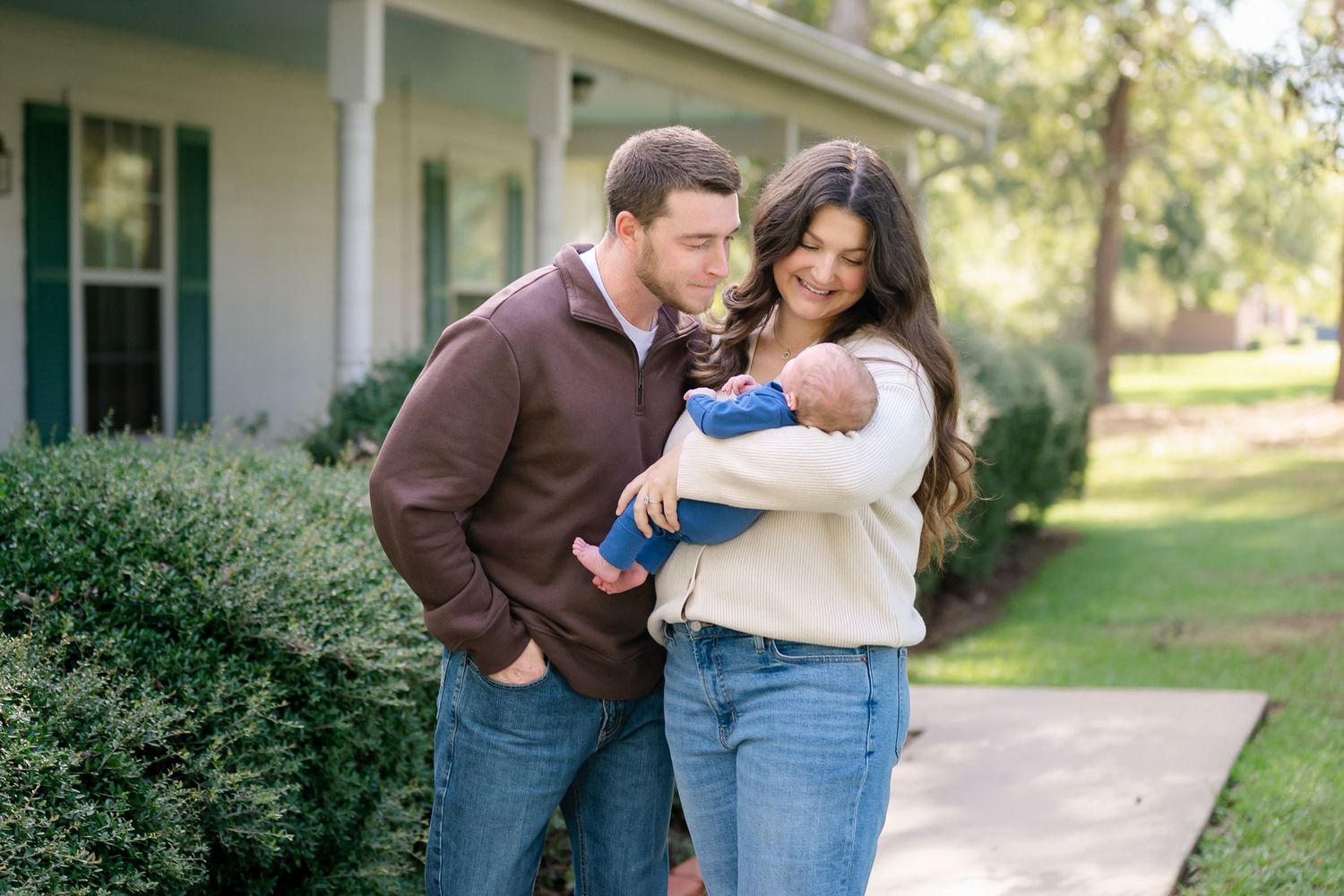 New parents smiling at their newborn son outside their Willis Tx home.