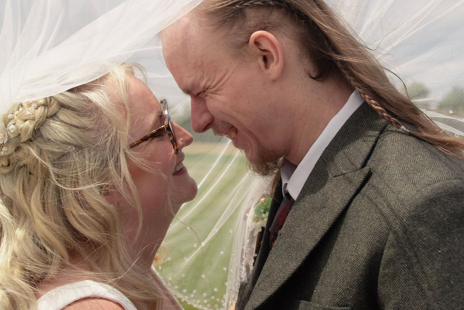 A joyful bride and groom share a laughing moment together under a flowing white veil on their wedding day.