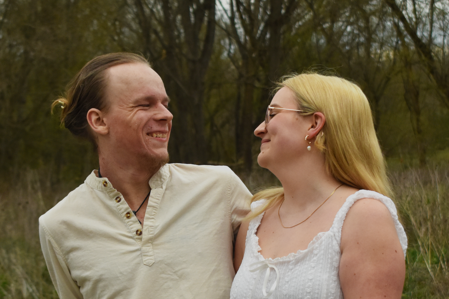 A smiling couple sharing a joyful moment outdoors, surrounded by lush greenery and trees in the background.