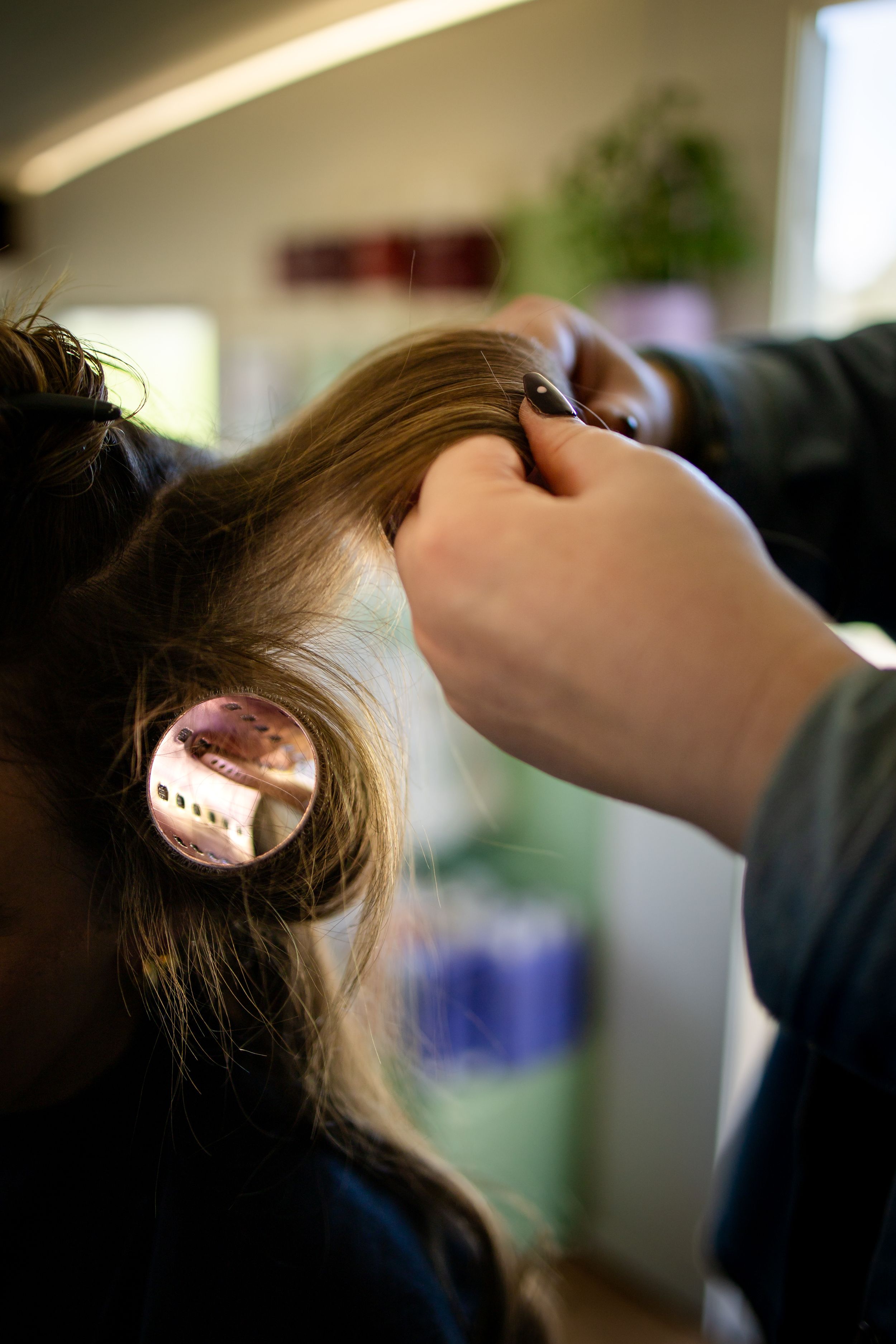 Hairstylist rolling a section of blonde hair onto a large curler in a professional salon setting.