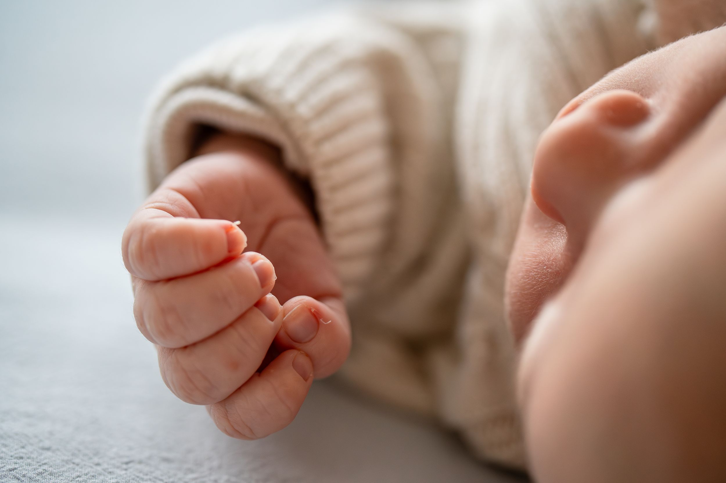 Close-up of a sleeping newborn baby's tiny clenched fist and ear, wearing a cozy knit sweater.