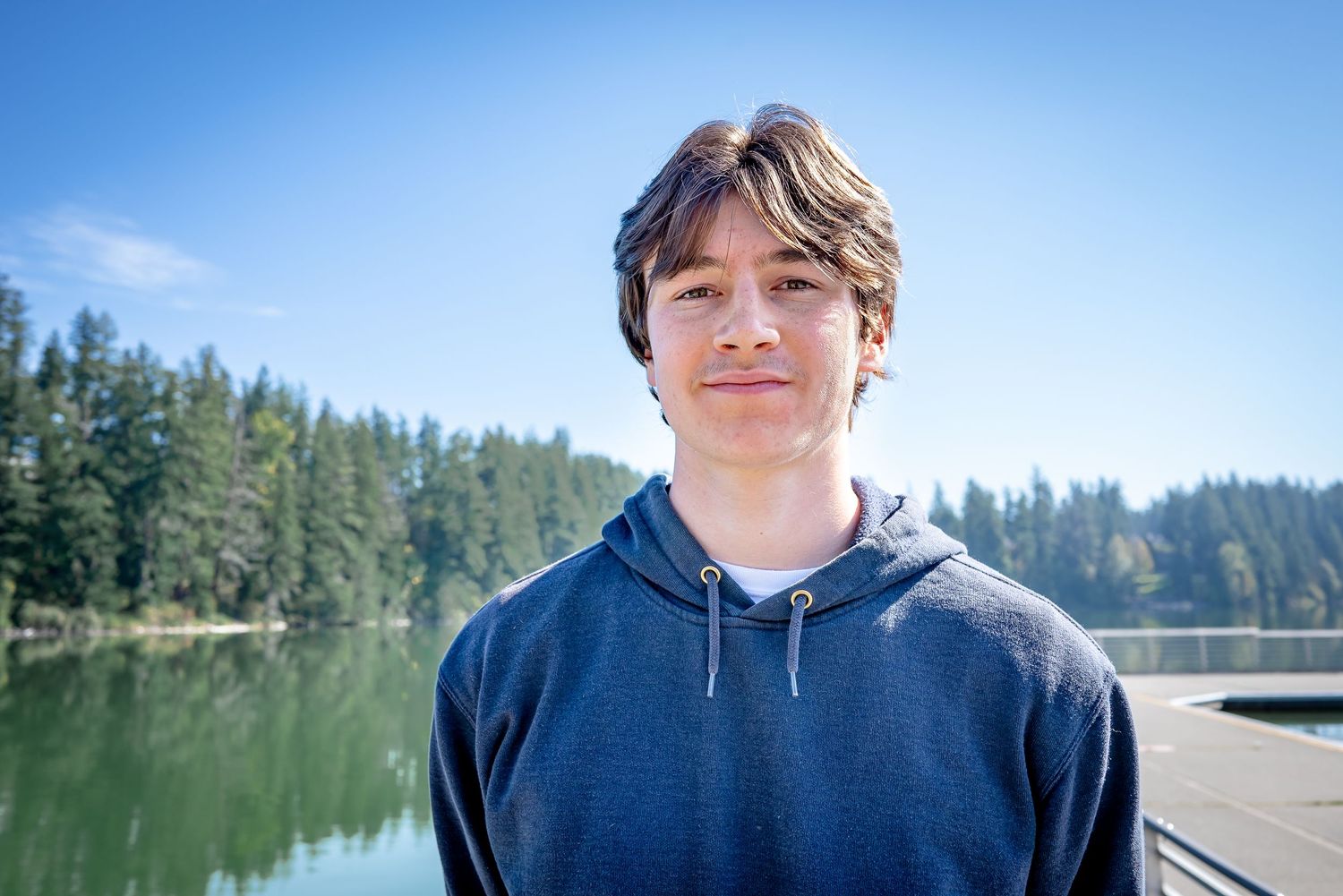 Close senior portrait with the lake, evergreens, and blue sky in the background