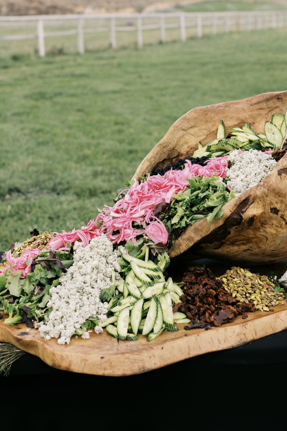 Stunning rustic salad display arranged in a large wooden bowl with fresh greens, cucumbers, pink onions, and seeds.