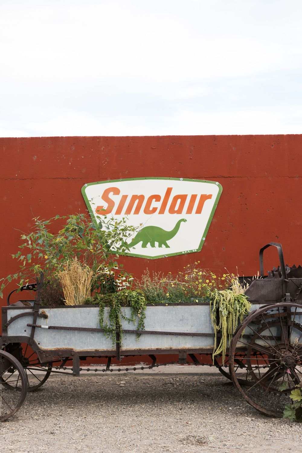 A vintage wagon planter sits in front of a red wall with a classic Sinclair gas station logo sign.
