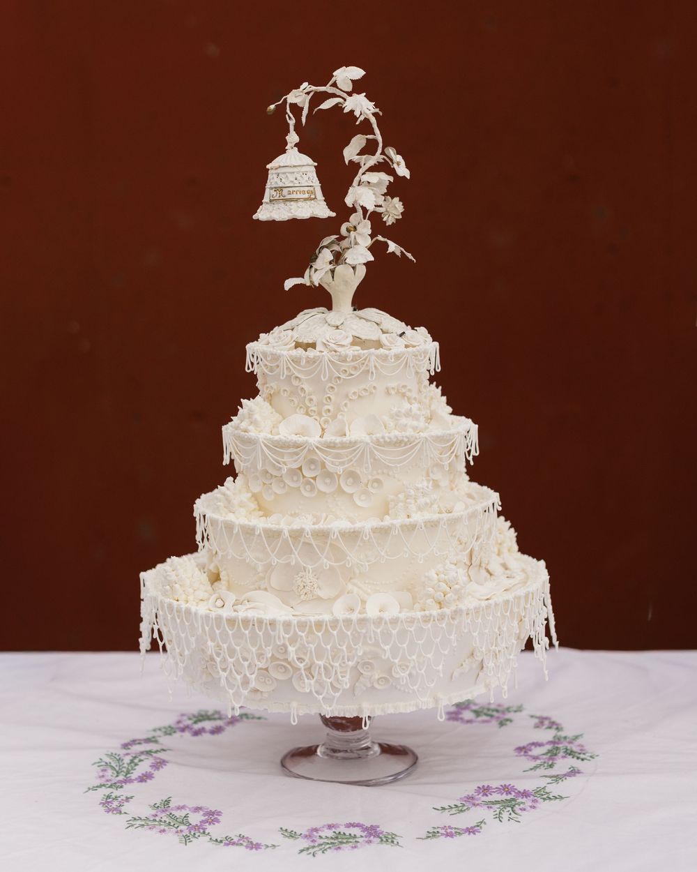 An elegant three-tiered white wedding cake with intricate lace details and a decorative floral topper.