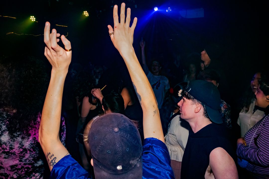 Concert crowd with raised hands dancing under blue stage lights at nightclub.