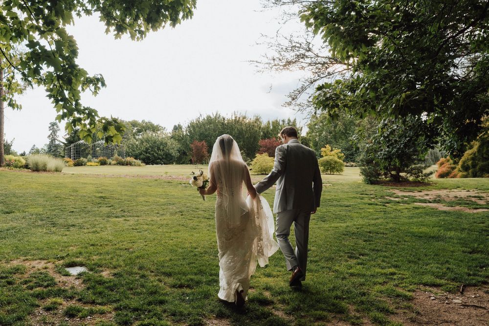 Bride and groom walking hand in hand through a lush green garden on their wedding day.