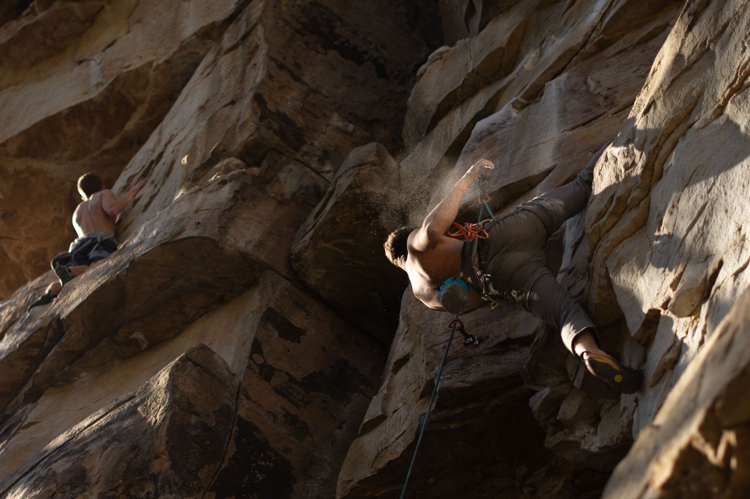 Rock climbers scale a steep cliff face with ropes and technical gear in dramatic lighting.