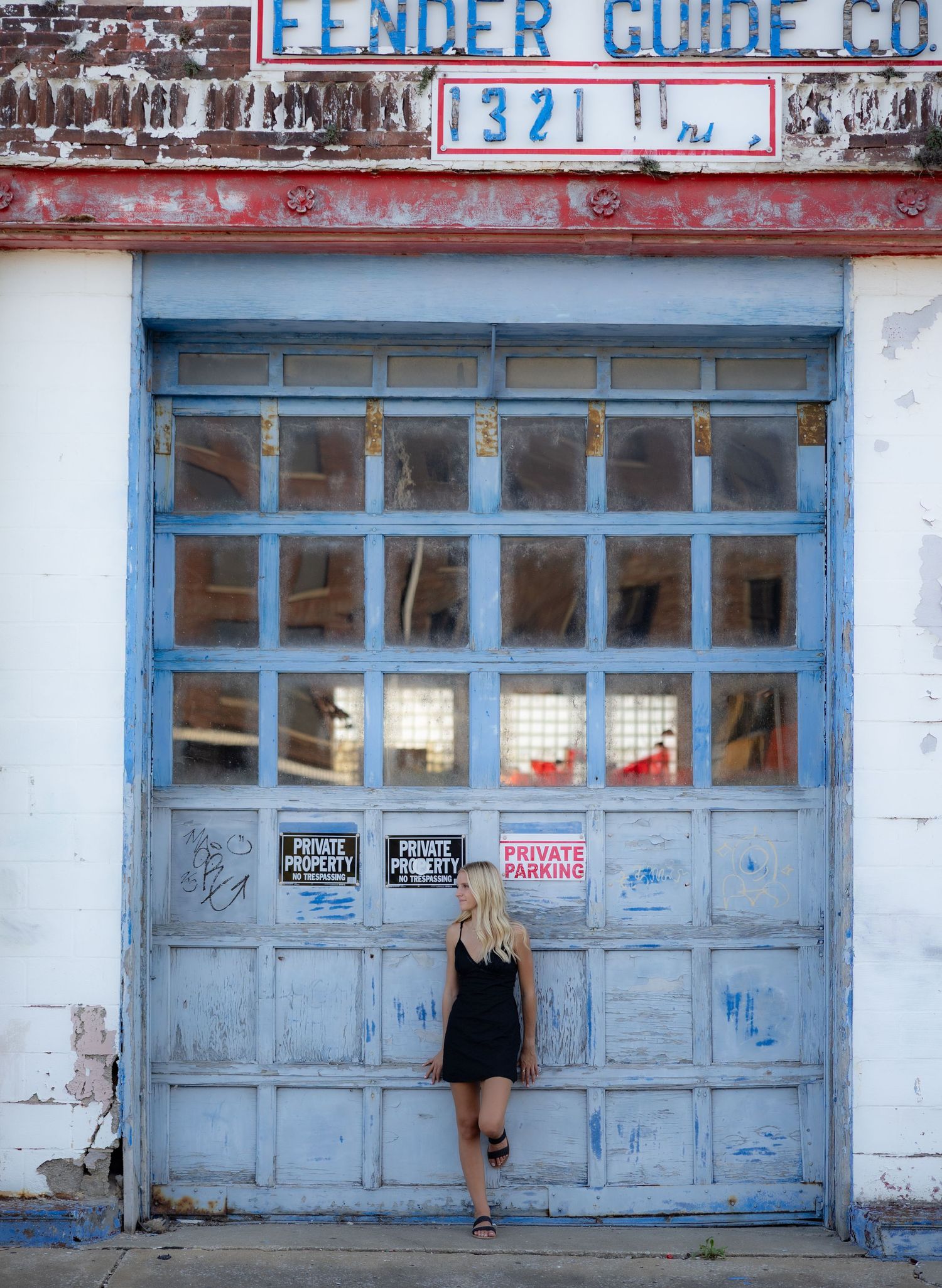 Blonde woman in black dress posing in front of vintage blue garage door at Fender Guide Co building 1321.