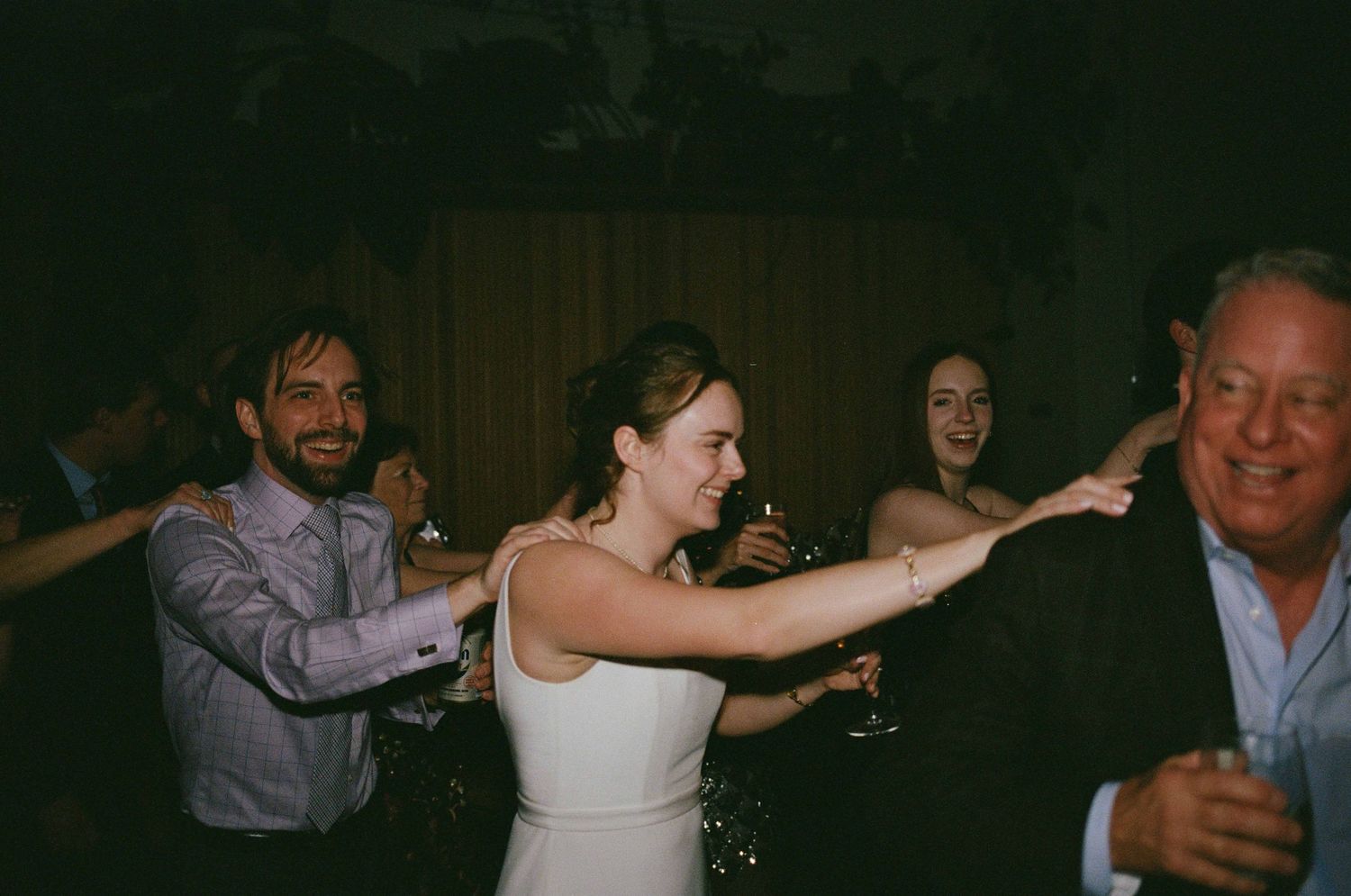 Bride in white dress dancing with guests at a lively wedding reception celebration.