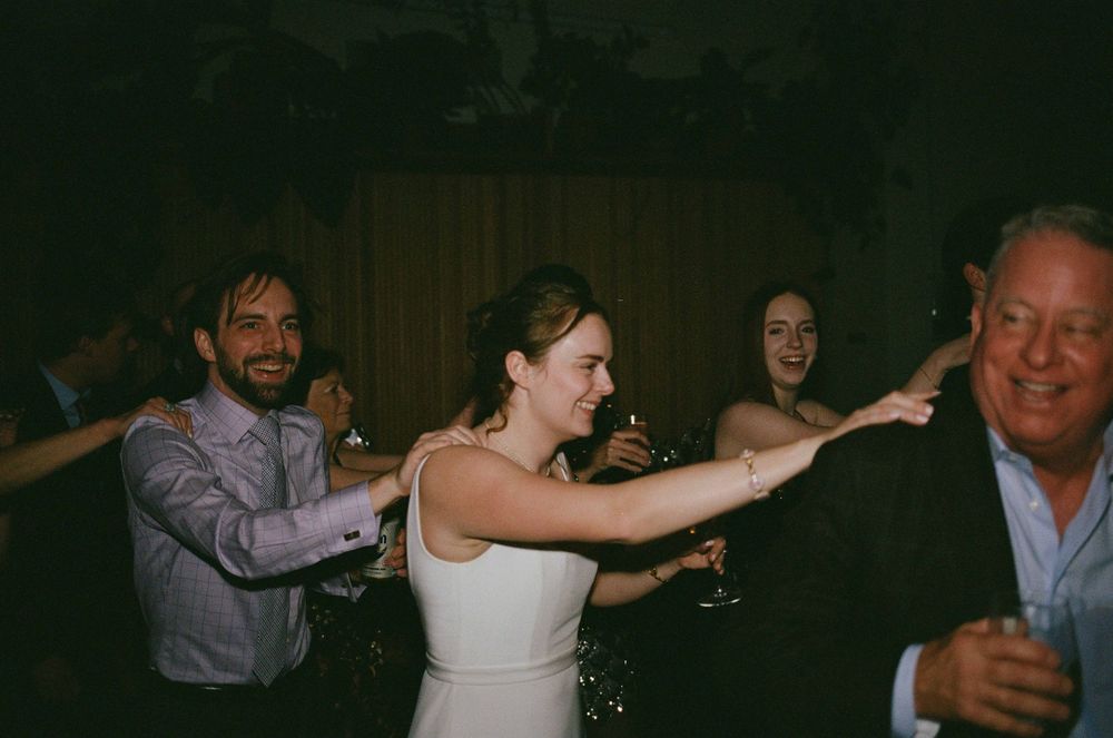 Bride in white dress dancing with guests at a lively wedding reception celebration.
