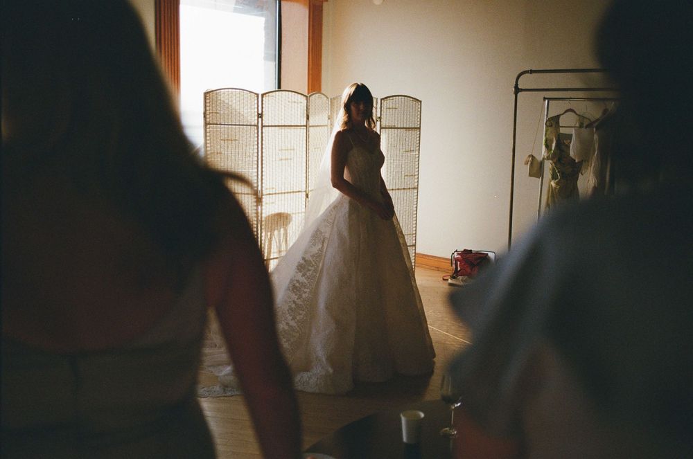 Bride in a white ball gown wedding dress standing in a sunlit room with a folding screen backdrop.