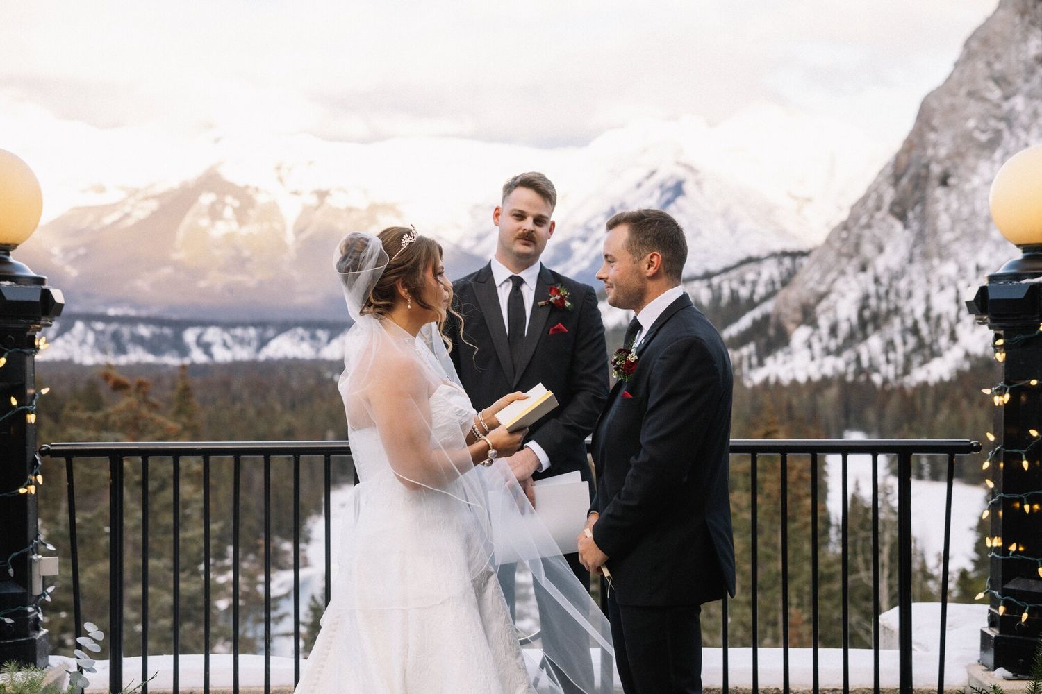 Bride reads from a small book as the groom smiles during their winter ceremony at the Fairmont Banff Springs