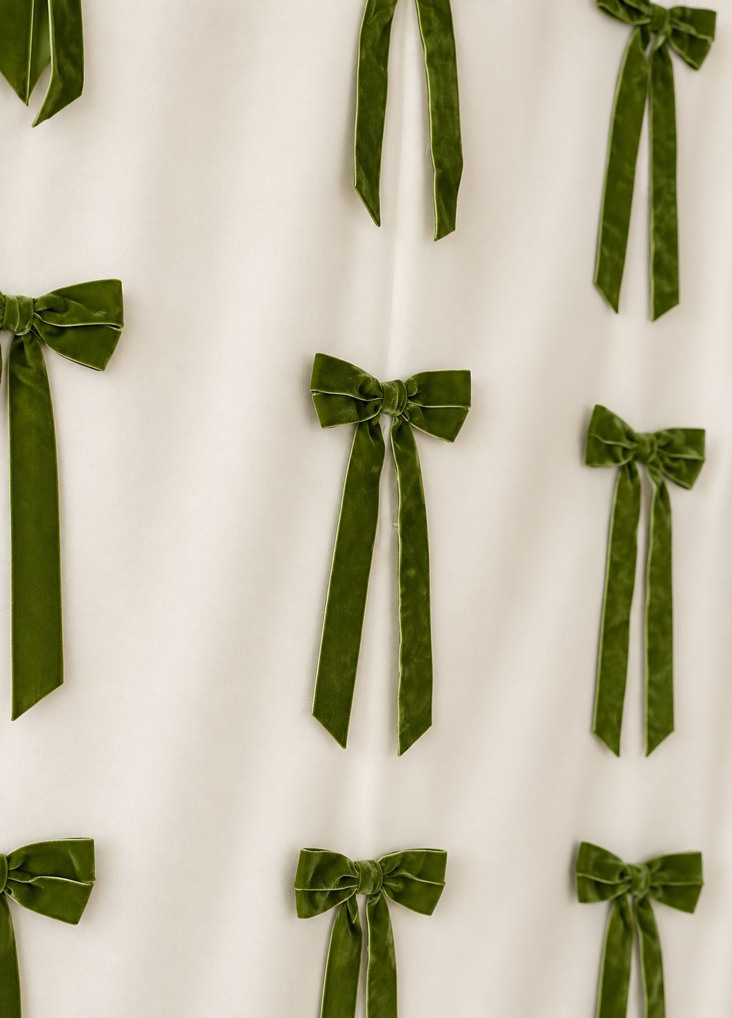 Green velvet bows arranged in a pattern on a white fabric backdrop, perfect for elegant holiday or wedding decor.