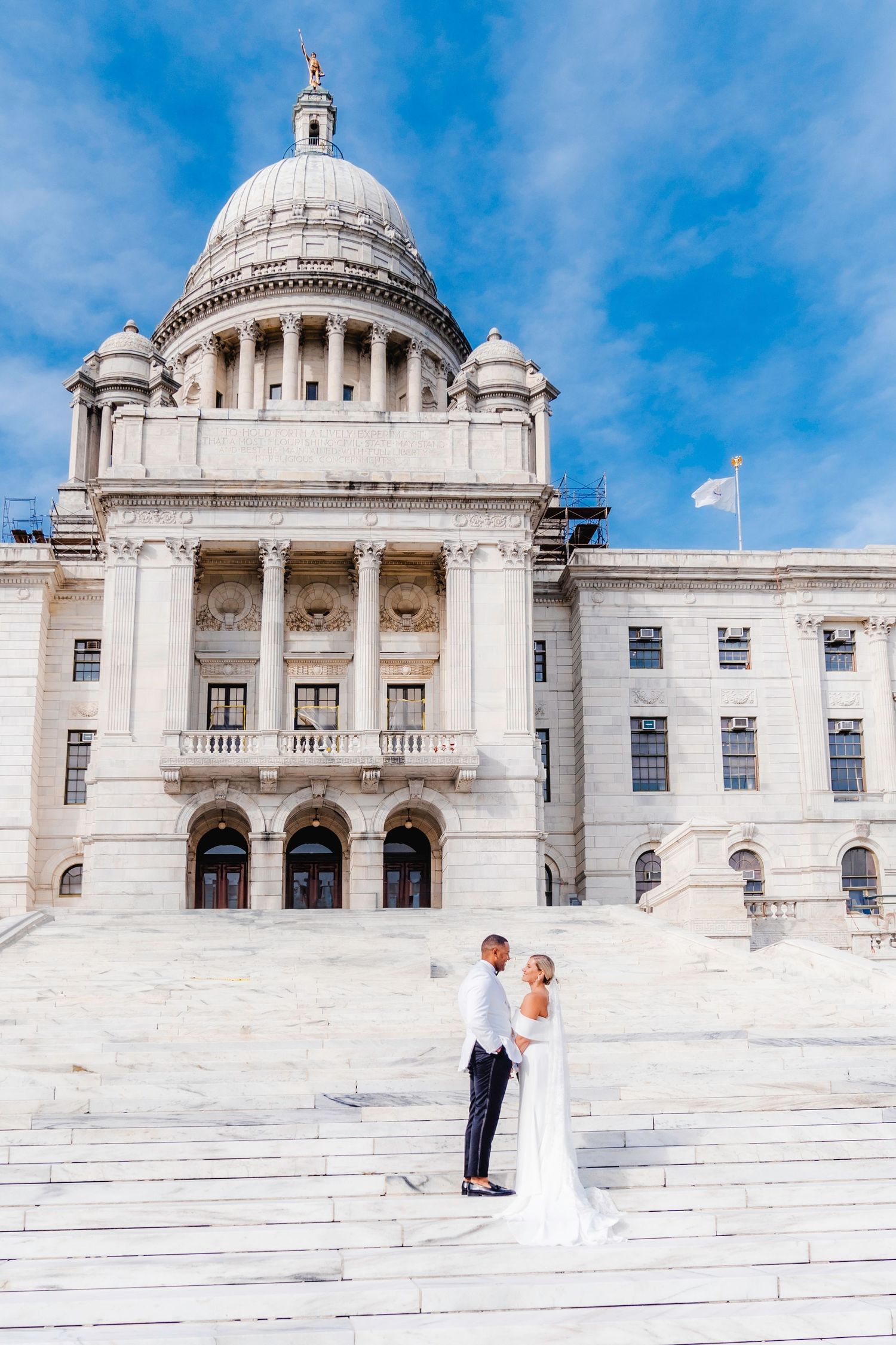 Wedding couple posing on grand steps of Rhode Island State House with neoclassical dome architecture.