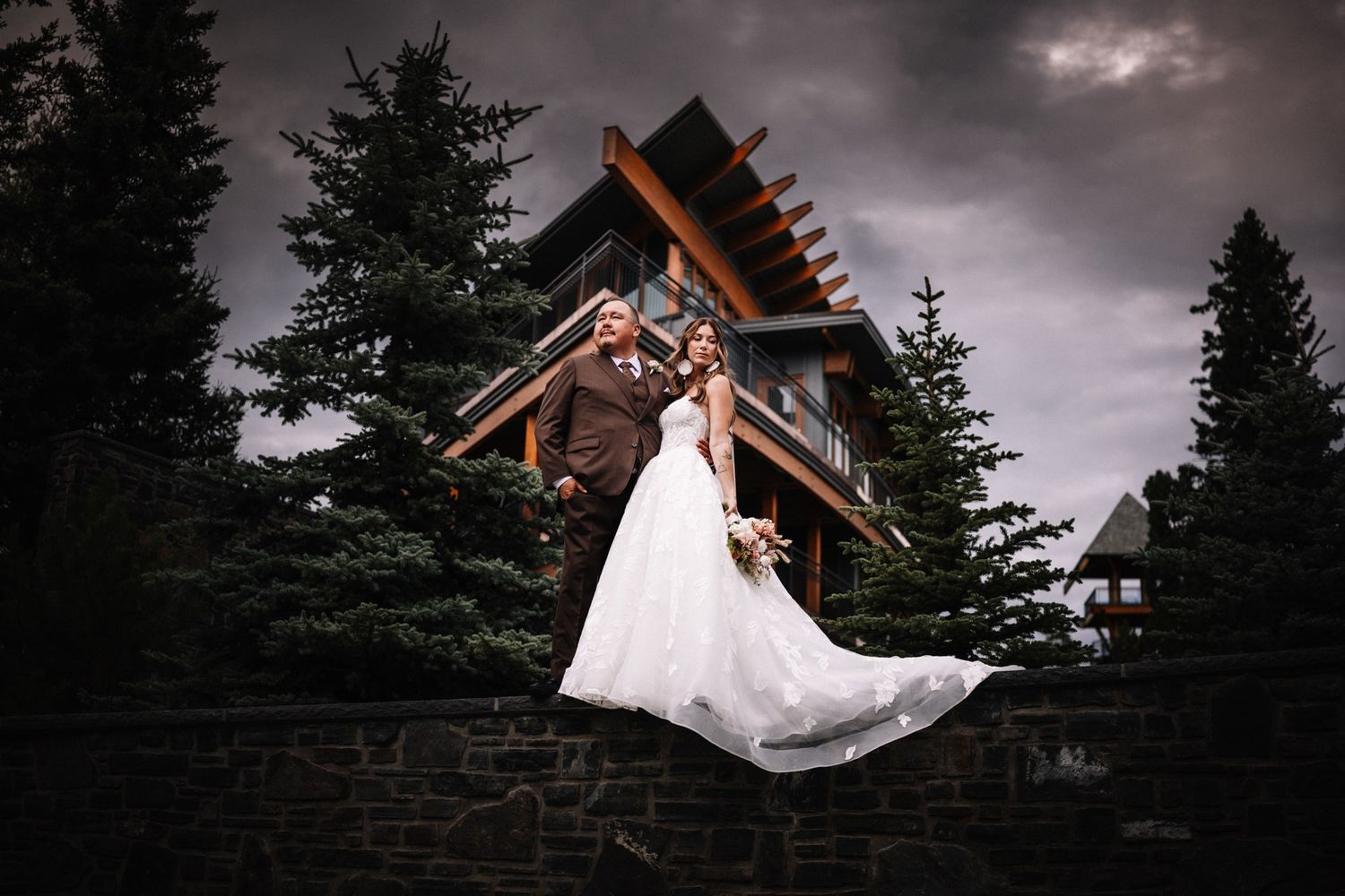 William Prince and Alyshia on the stone wall in front of Azuridge Estate Hotel under a stormy sky