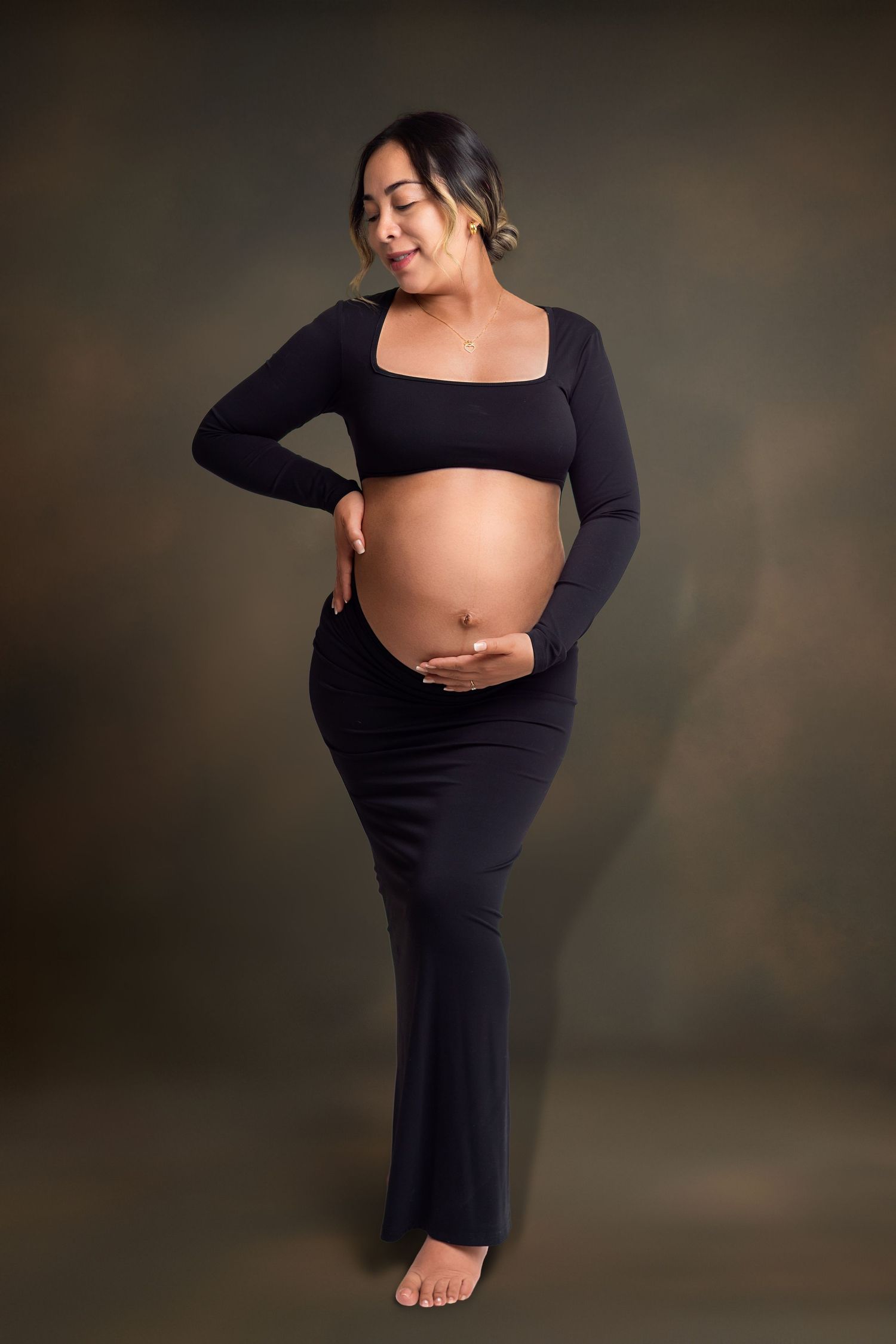 Pregnant woman in black crop top and maxi skirt cradling baby bump during professional maternity photo session.