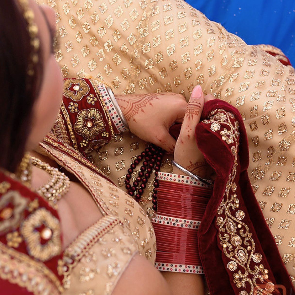 A couple in traditional Indian attire share a tender embrace, the woman smiling in gold jewelry and green outfit.