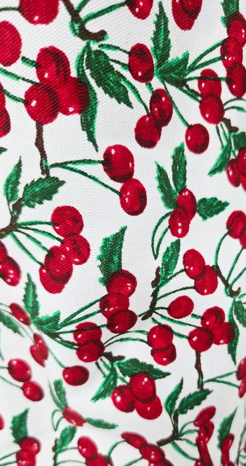 Red cherry print fabric with green leaves on white background, perfect for retro-inspired sewing projects.