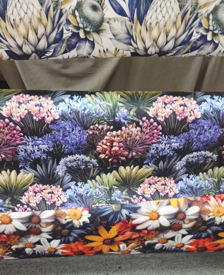 Three stacked floral fabric rolls featuring protea, hydrangea, agapanthus, and daisy prints in vibrant colors.