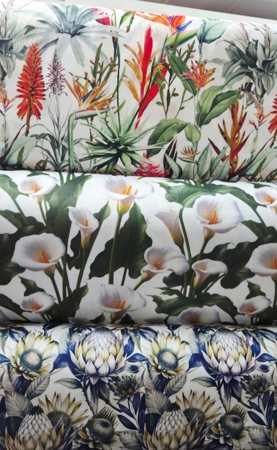 Three rolled fabric bolts featuring vibrant floral prints including tropical flowers, white calla lilies, and blue proteas.