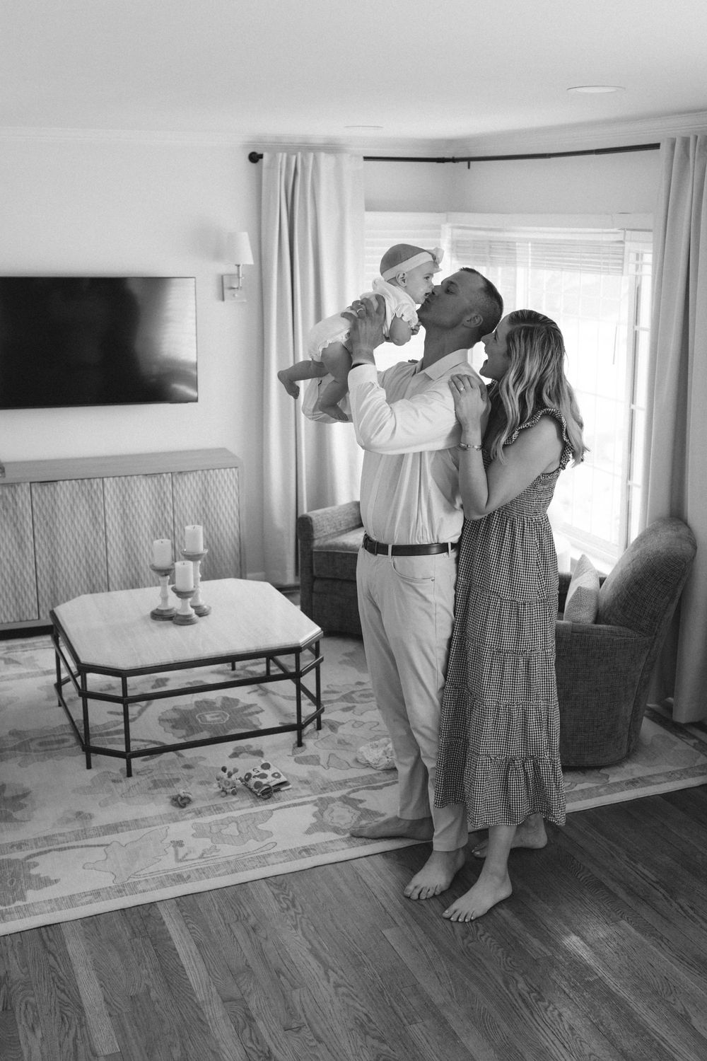 Black and white photo of parents lifting newborn baby in cozy living room.