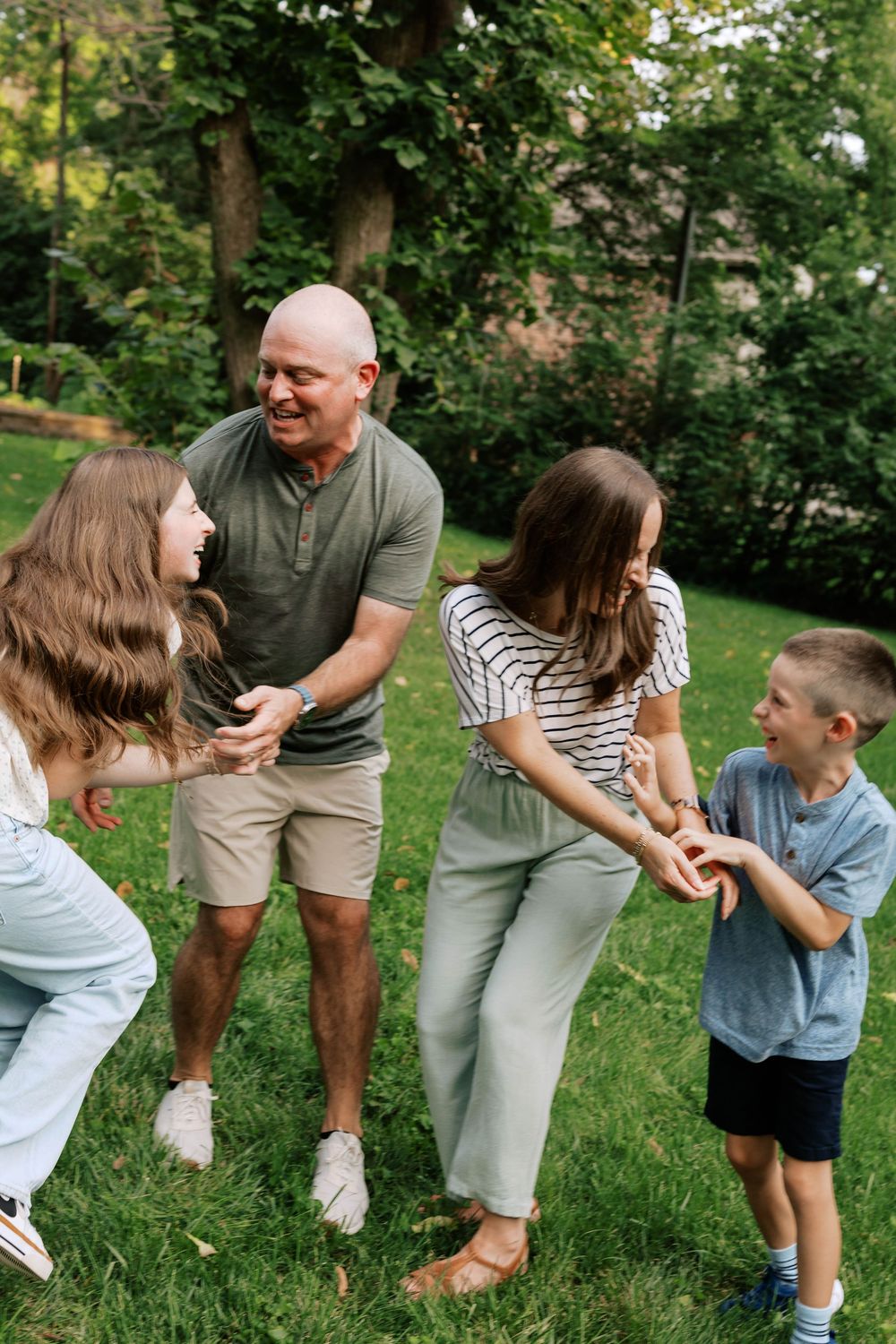 Active family of five playing together in lush green backyard on sunny summer day.