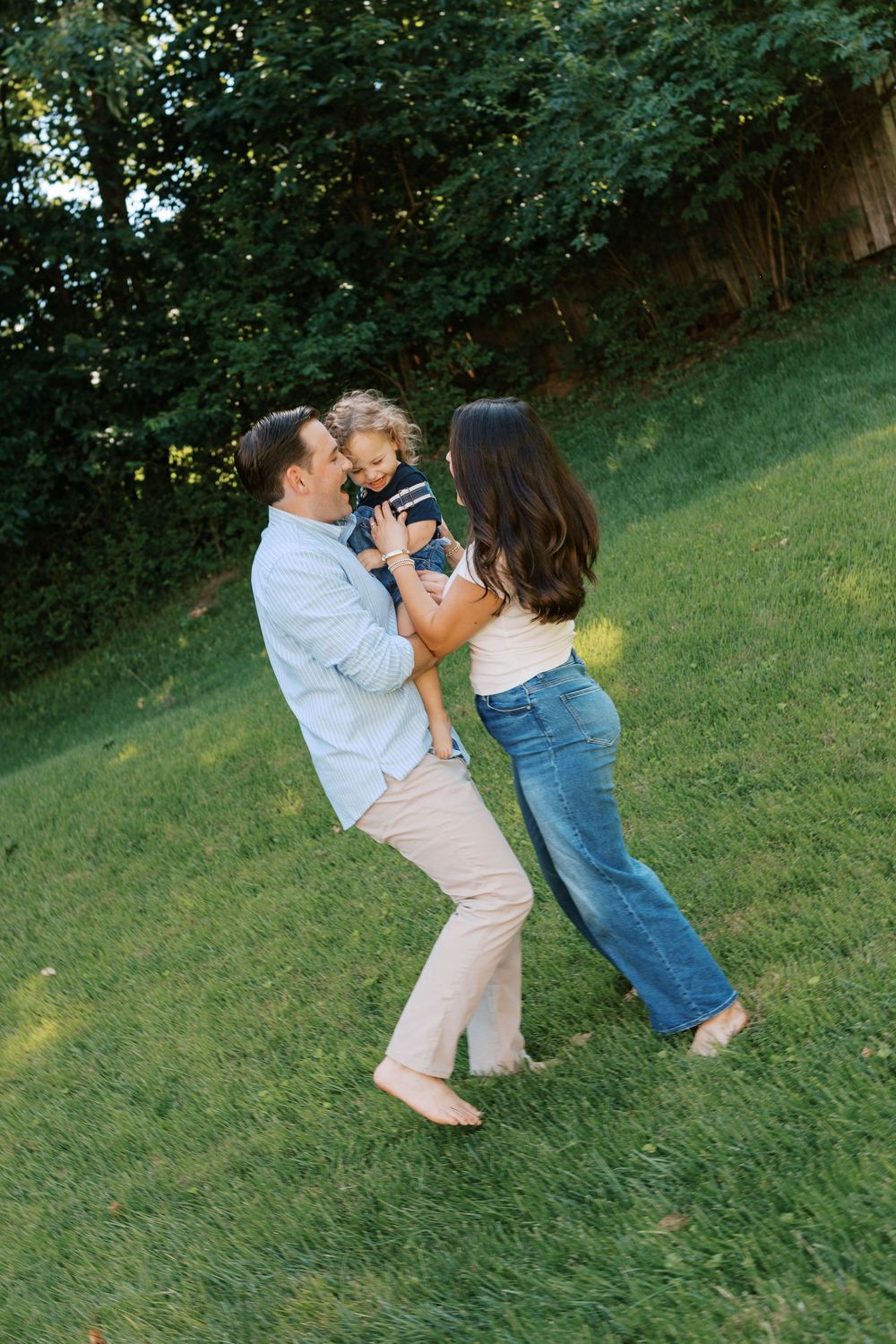 Happy family with toddler playing outdoors on lush green grass in warm summer light.