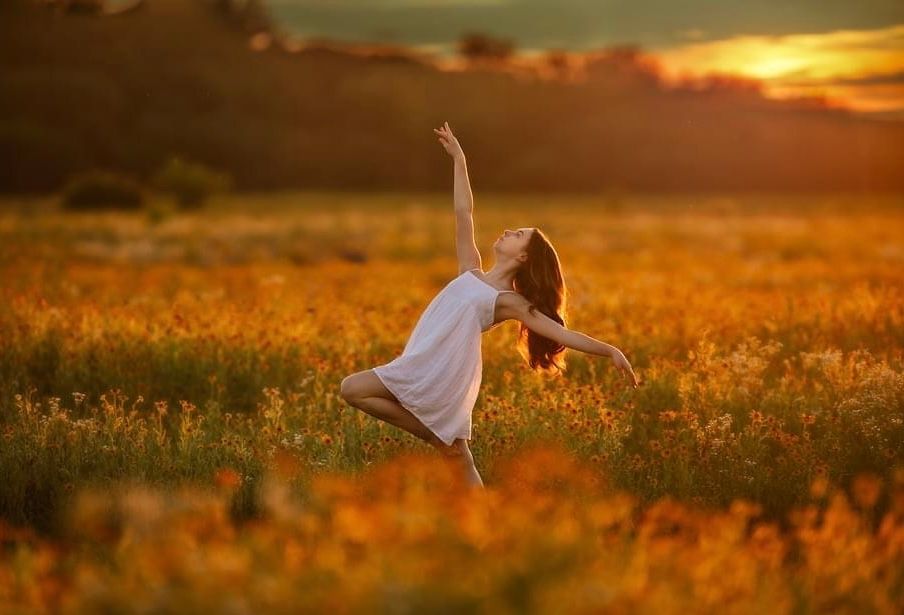 A graceful dancer leaps in a golden sunset field wearing a white dress.