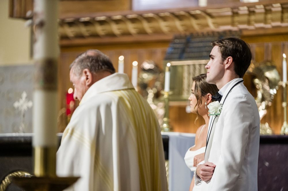 Bride and groom stand at church altar during wedding ceremony with priest in gold vestments.