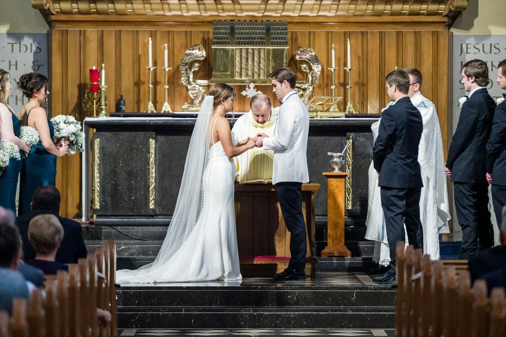 Bride and groom exchanging vows at a church altar during a traditional wedding ceremony with bridal party.