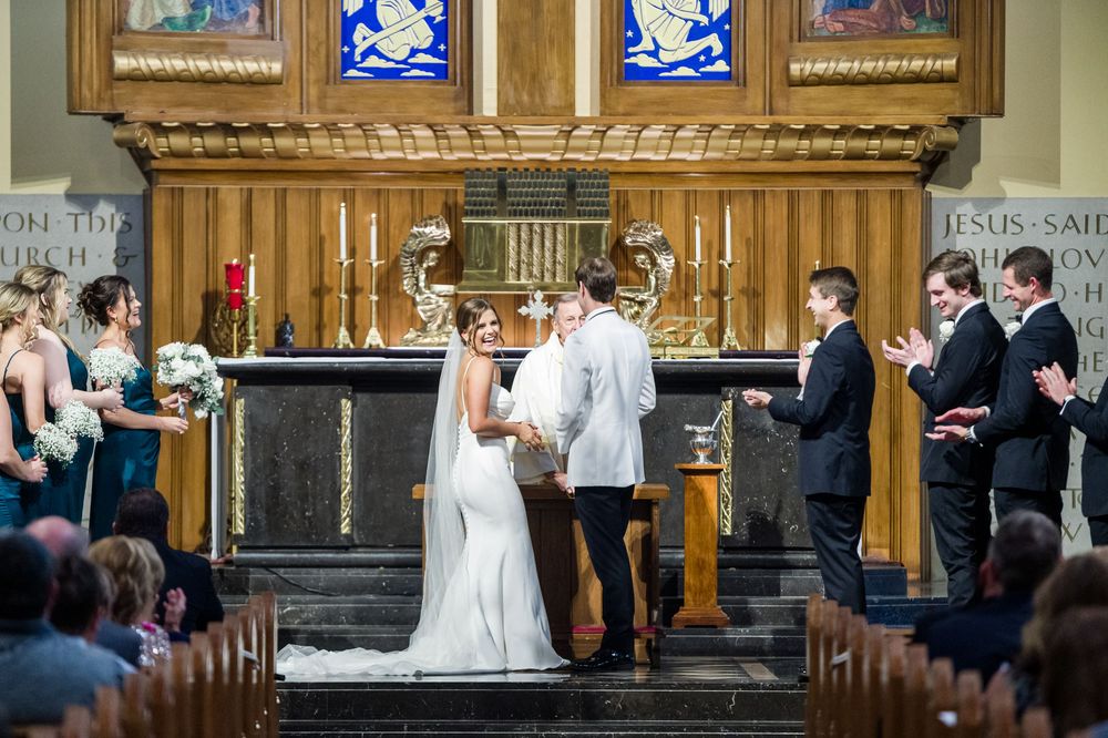 Bride and groom exchange vows at a church altar, surrounded by bridesmaids and groomsmen during a wedding ceremony.