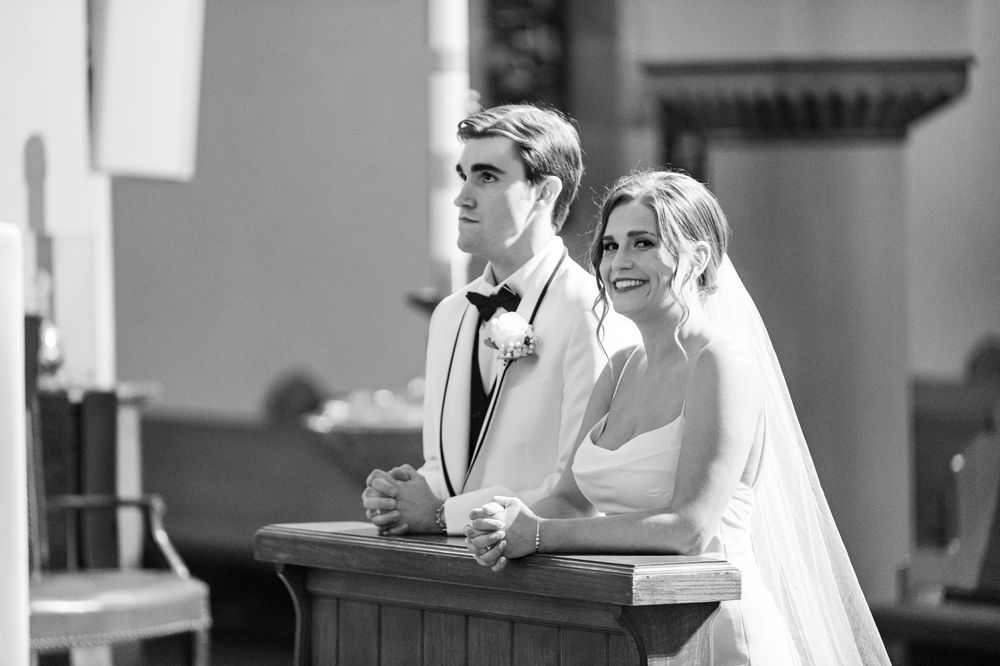 Black and white photo of a bride and groom kneeling at church altar during their wedding ceremony.